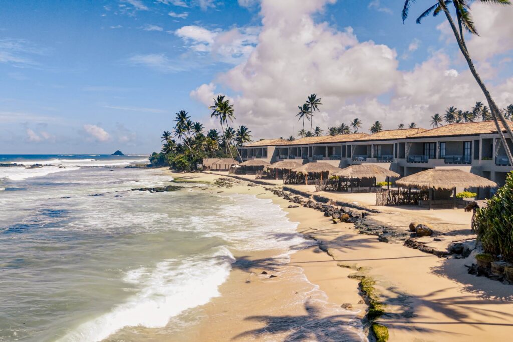Beachfront resort beside the Indian Ocean, with coconut palms and waves along the Sri Lankan coast